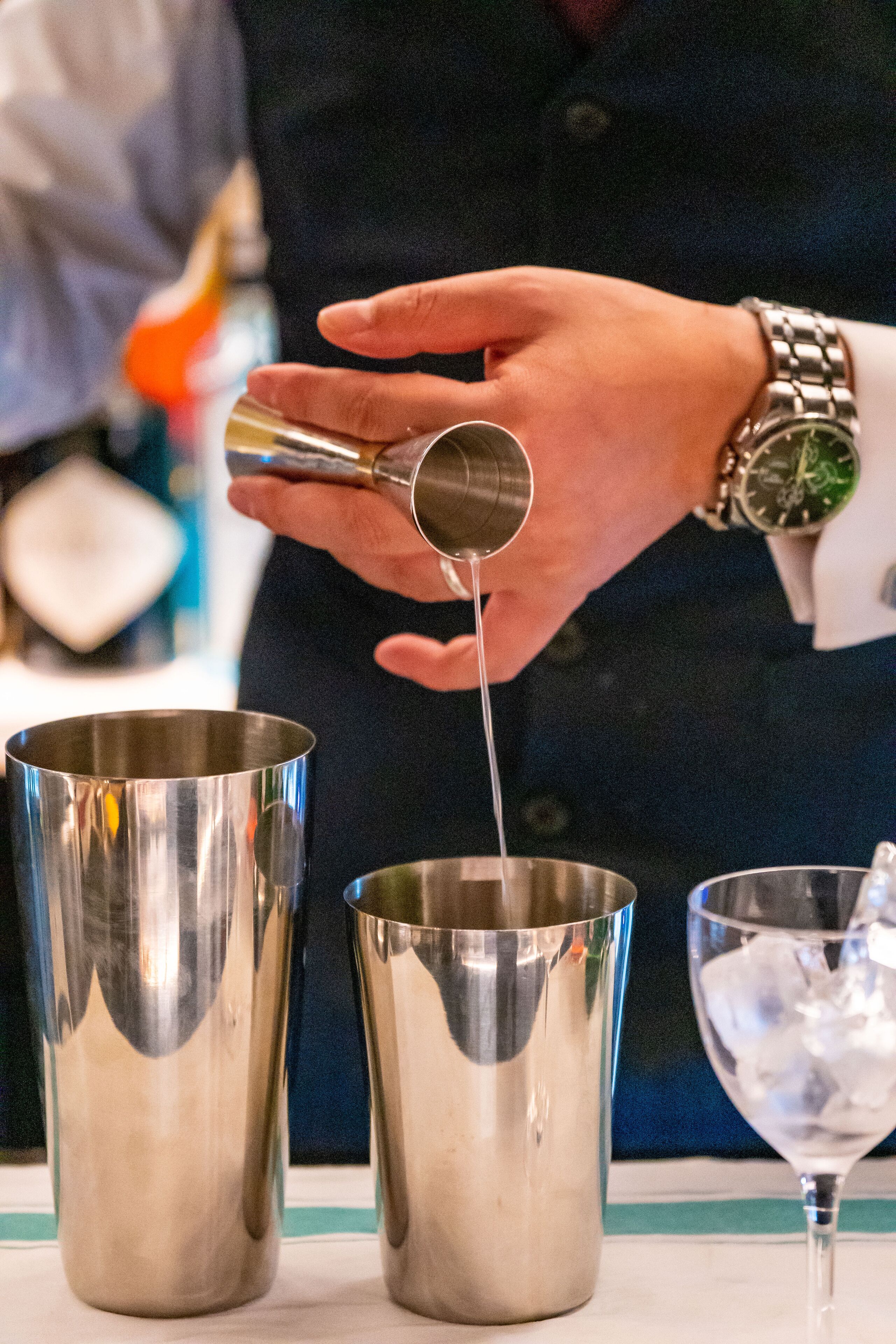 A person pouring a liquid from a small container into a metal cup.