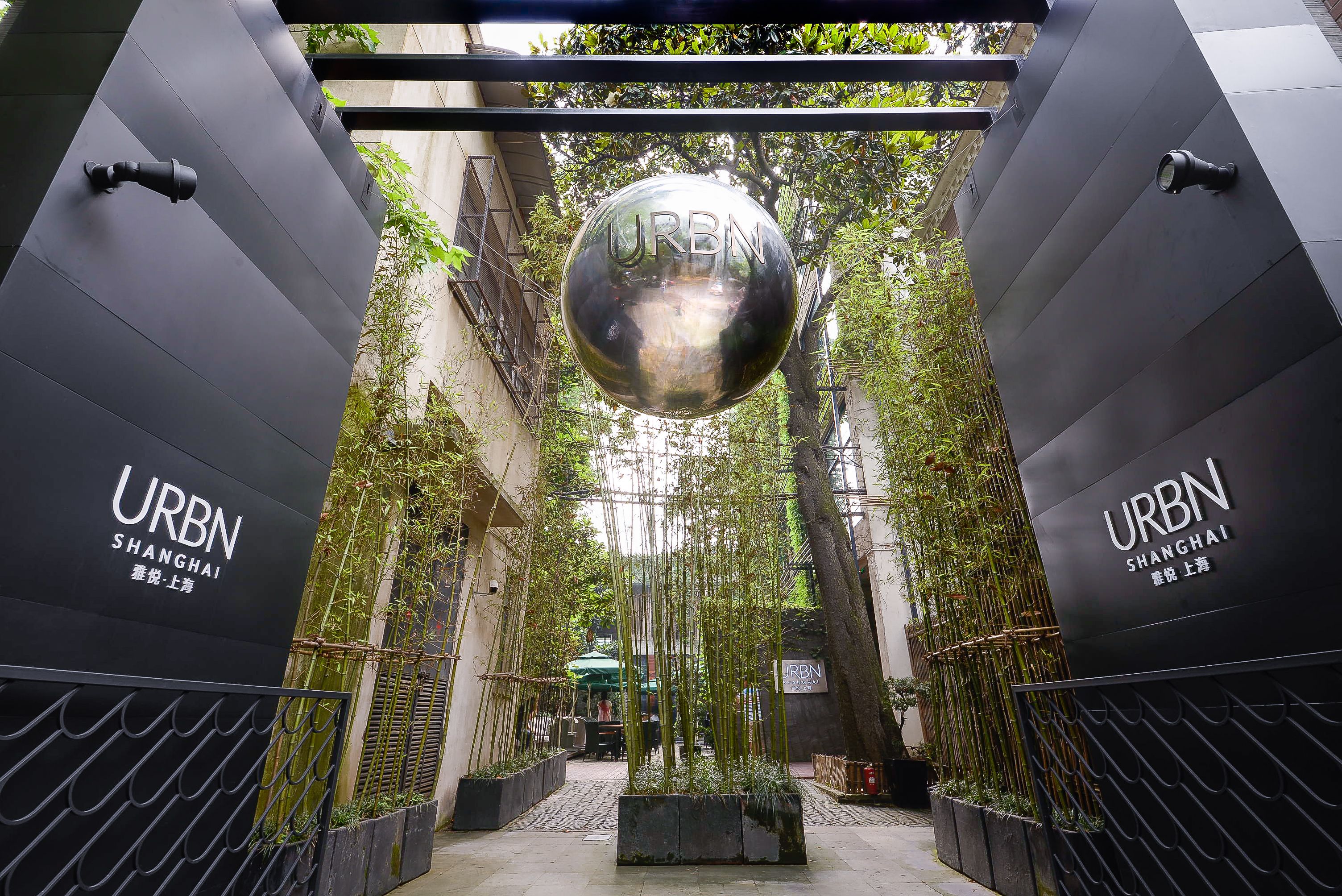 A modern entrance with a spherical sculpture, black walls, and greenery.