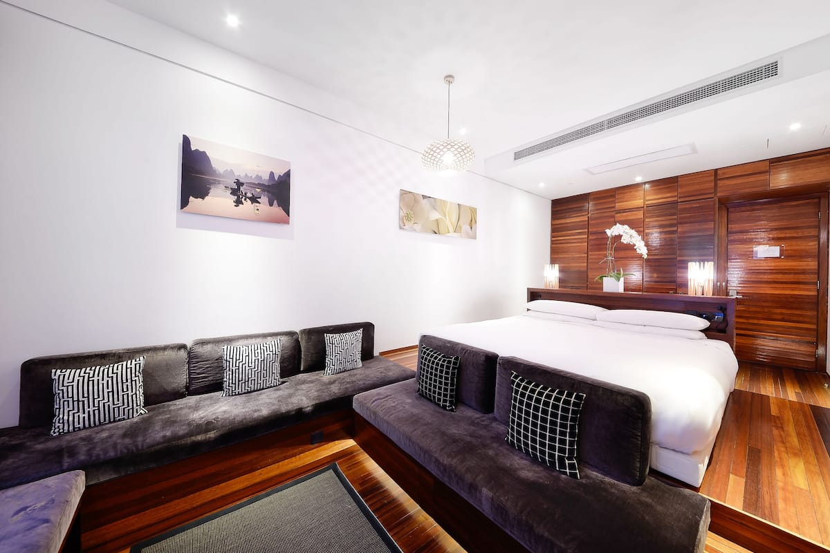 A modern hotel room with a large bed, a sofa, and a wooden accent wall.