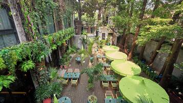 An outdoor café area with tables and chairs, surrounded by lush greenery and trees.