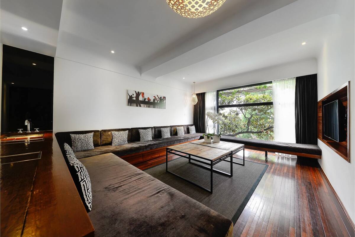A modern living room with a large sectional sofa, a coffee table, and a TV mounted on the wall.