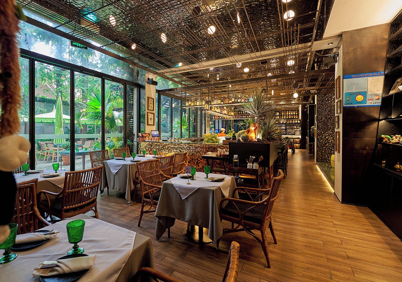 Interior de un restaurante con mesas, sillas, una zona de bar y grandes ventanales con vistas a zonas verdes.