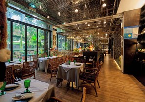 A restaurant interior with tables and chairs, a bar area, and large windows with a view of greenery. - URBN Boutique Shanghai (Shanghai)