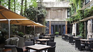 Ein Straßencafé mit Tischen und Stühlen, ein überdachter Sitzbereich und ein Gebäude im Hintergrund.