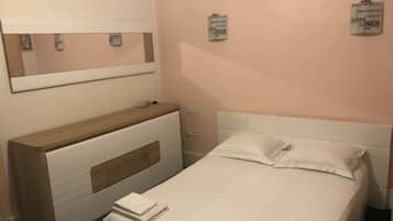 Een hotelkamer met een bed, een houten nachtkastje, een spiegel en een muur met een bord waarop steden staan vermeld.