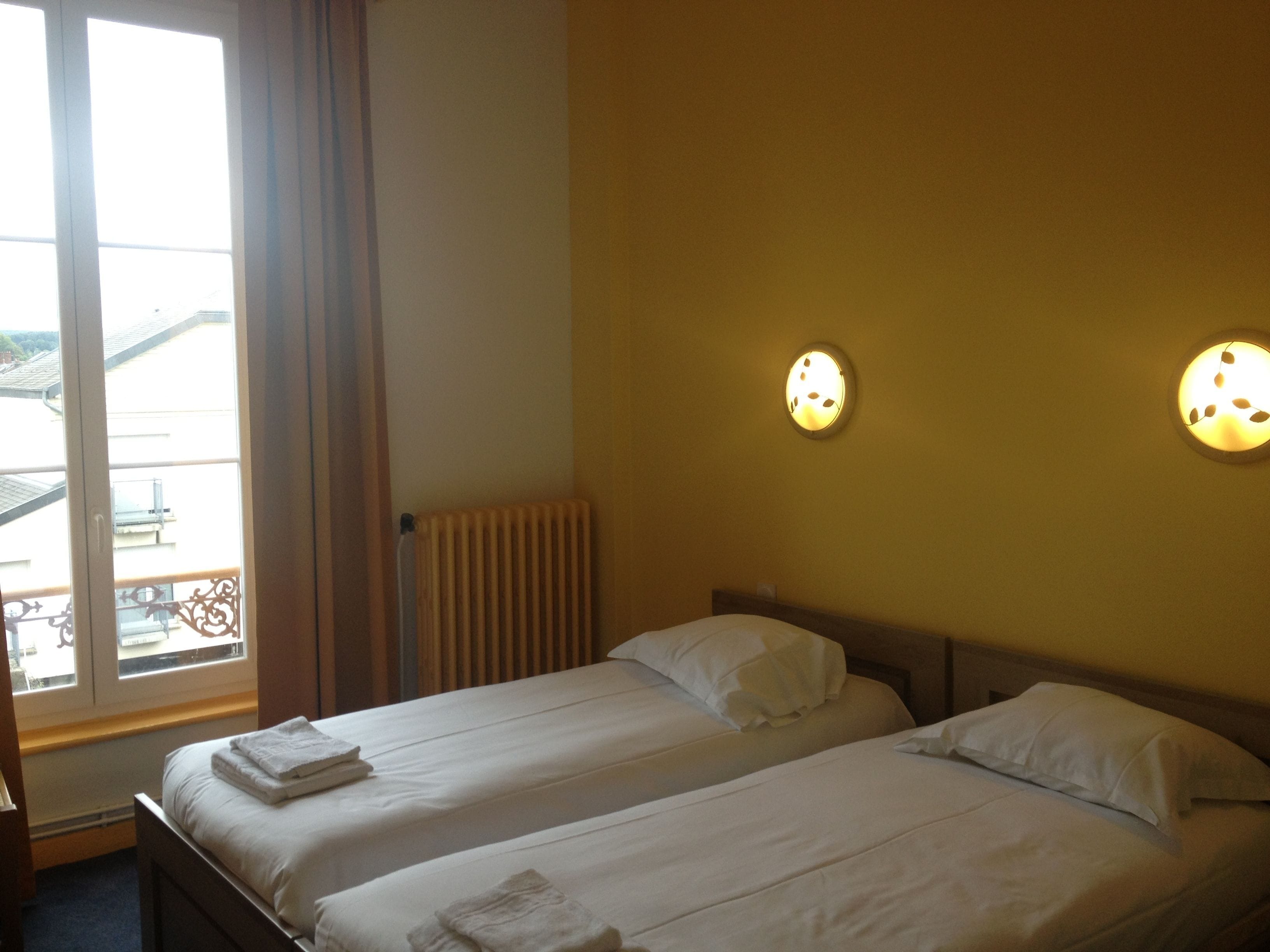 A hotel room with two beds, a radiator, and a window with curtains.