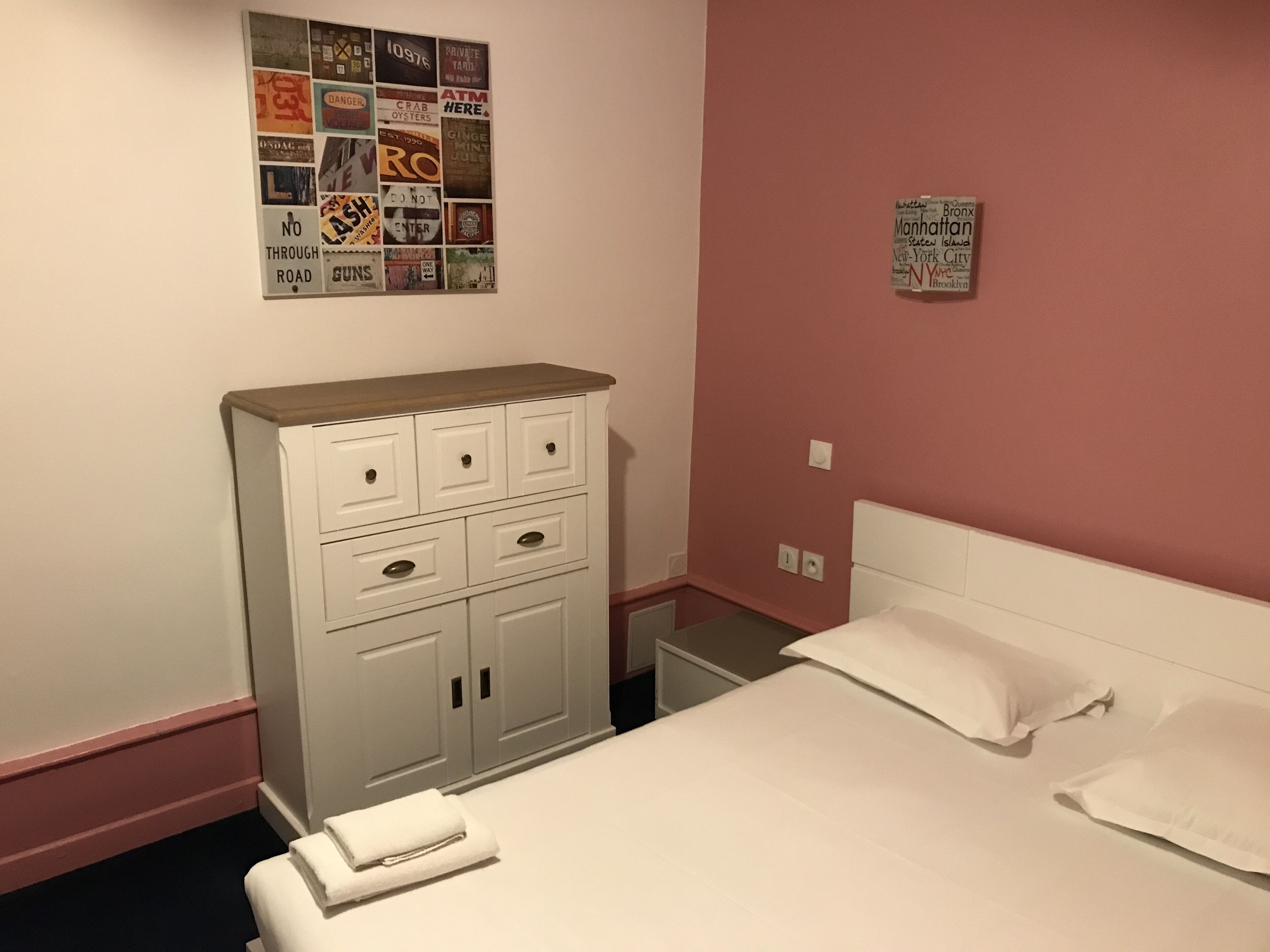 Ein Schlafzimmer mit Bett, Kommode, Nachttisch und einer Wand mit verschiedenen Postern.