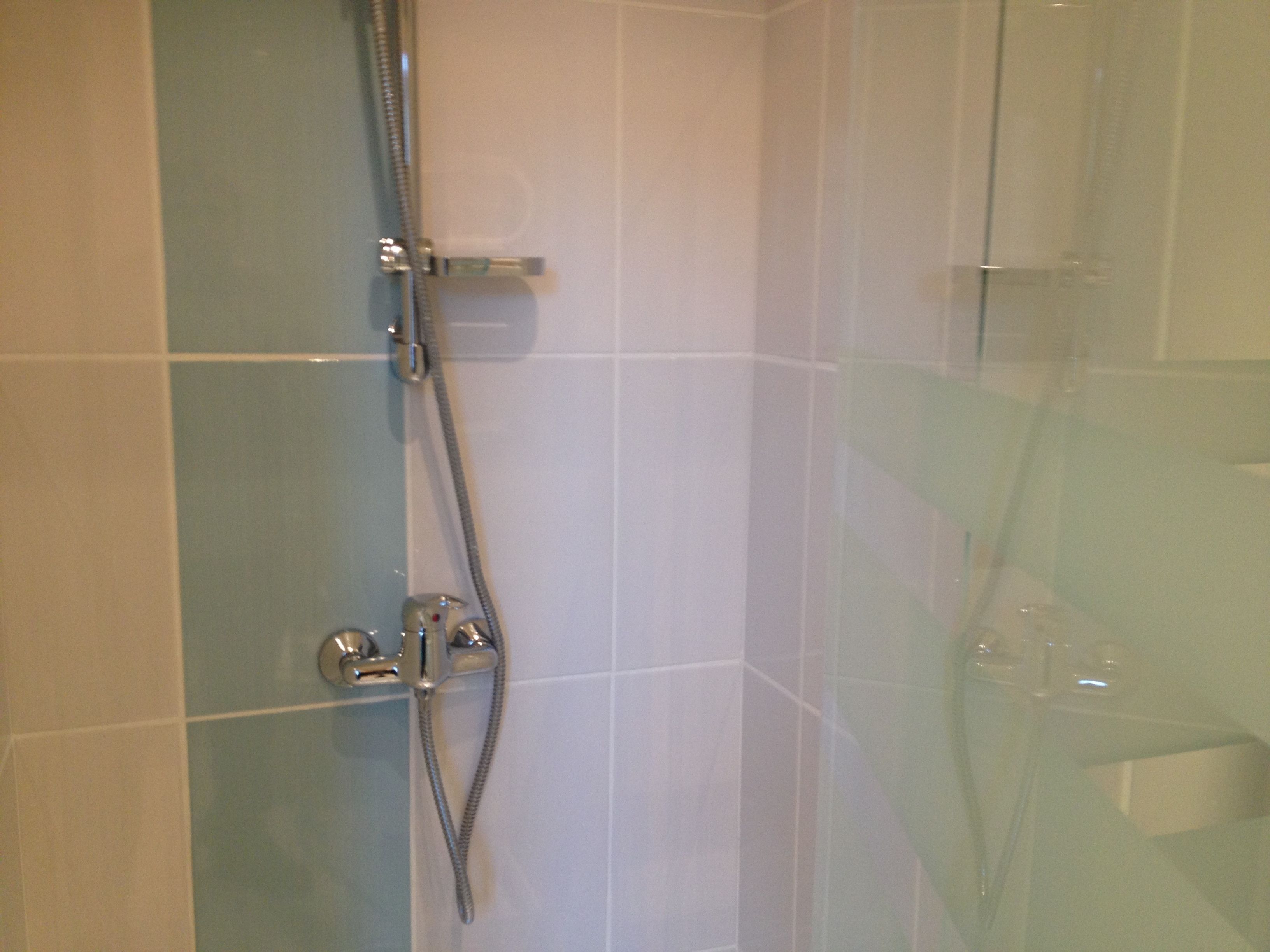 Zona de ducha con mampara de vidrio, ducha de mano y grifo empotrado en la pared.