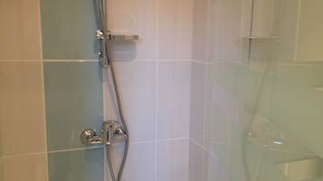 Zona de ducha con mampara de vidrio, ducha de mano y grifo empotrado en la pared.