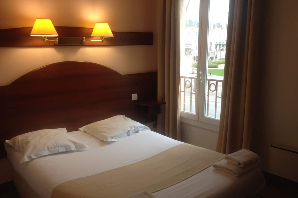 Une chambre d’hôtel avec un grand lit, deux lampes de chevet, une vue sur le balcon extérieur et une fenêtre avec des rideaux.