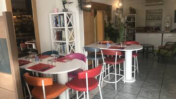 Een eethoek met ronde tafels en stoelen, een boekenkast en een televisie.