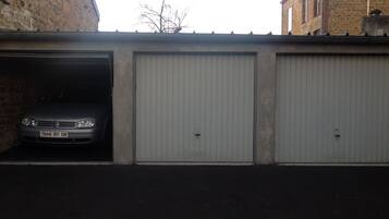 Un edificio con tres puertas de garaje, una de ellas abierta mostrando un coche estacionado.