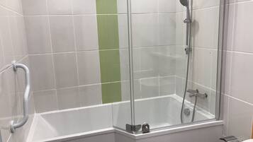 Un área de ducha con paredes de vidrio, una bañera blanca, una franja vertical verde en la pared y un pasamanos.