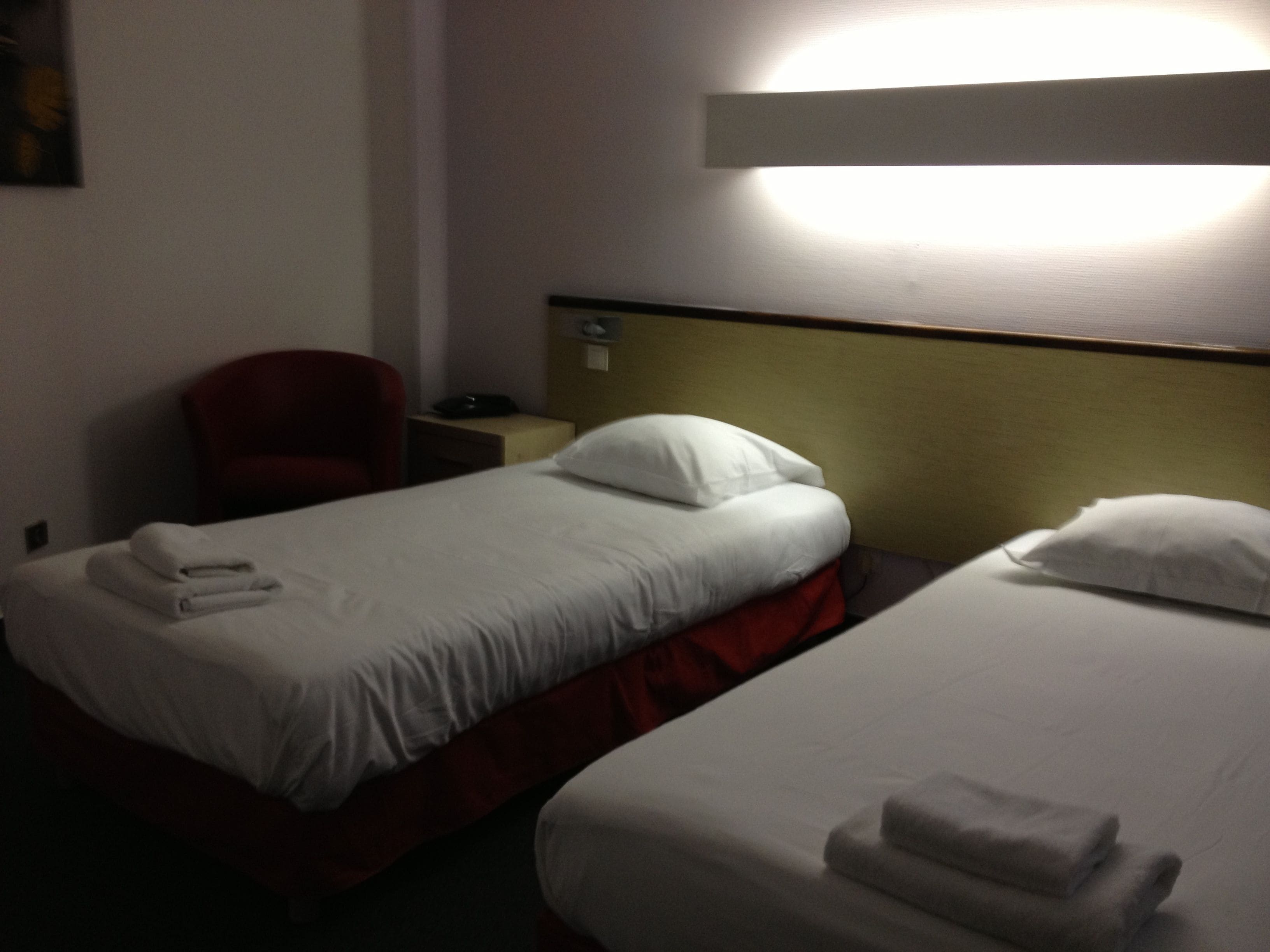 A hotel room with two beds, a chair, and a nightstand with a lamp.
