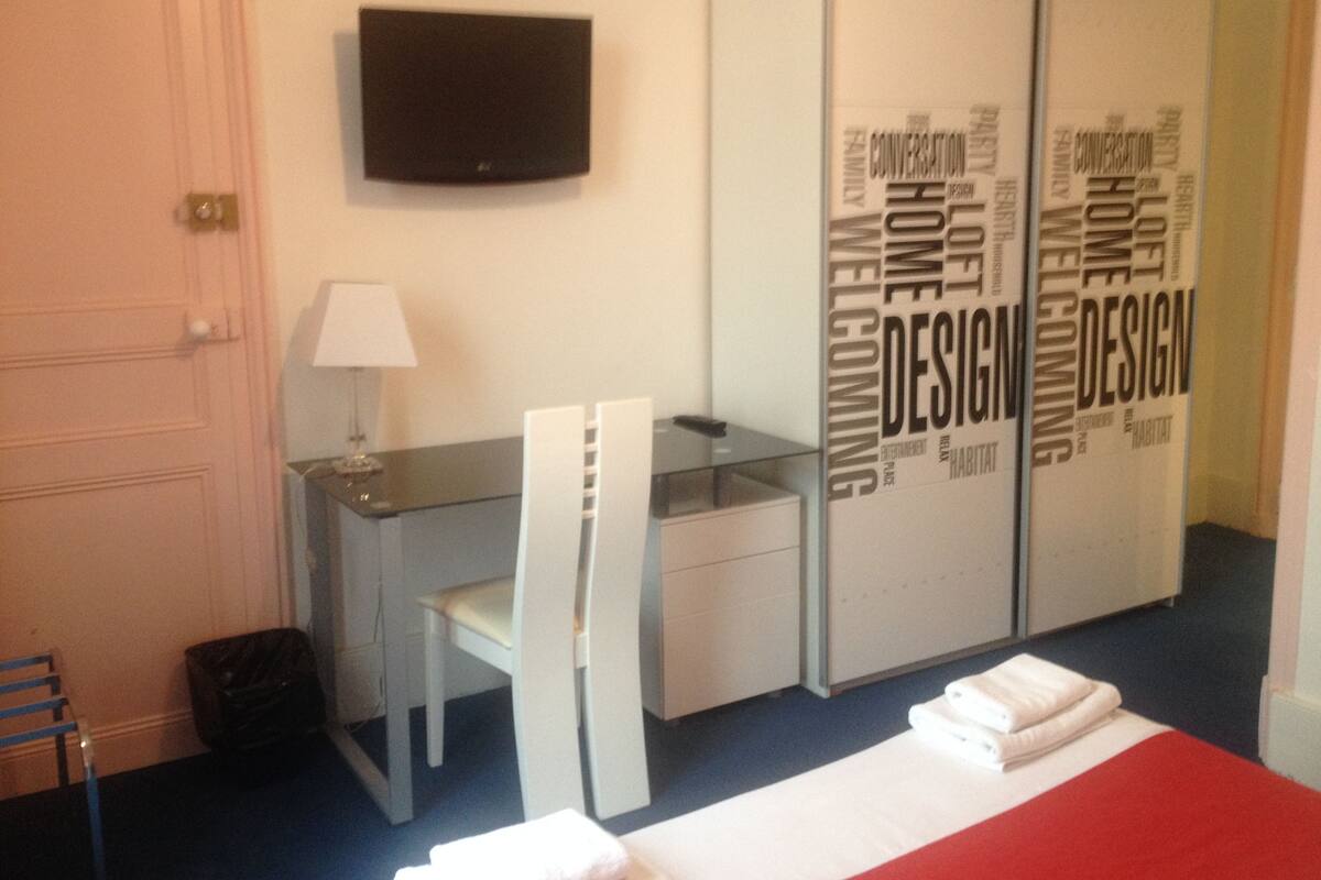 Une chambre d’hôtel équipée d’un bureau, de chaises, d’une télévision et d’une armoire sur laquelle est inscrit le mot « Design ».