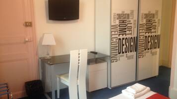 A hotel room with a desk, chairs, a television, and a wardrobe with 'Design' written on it.