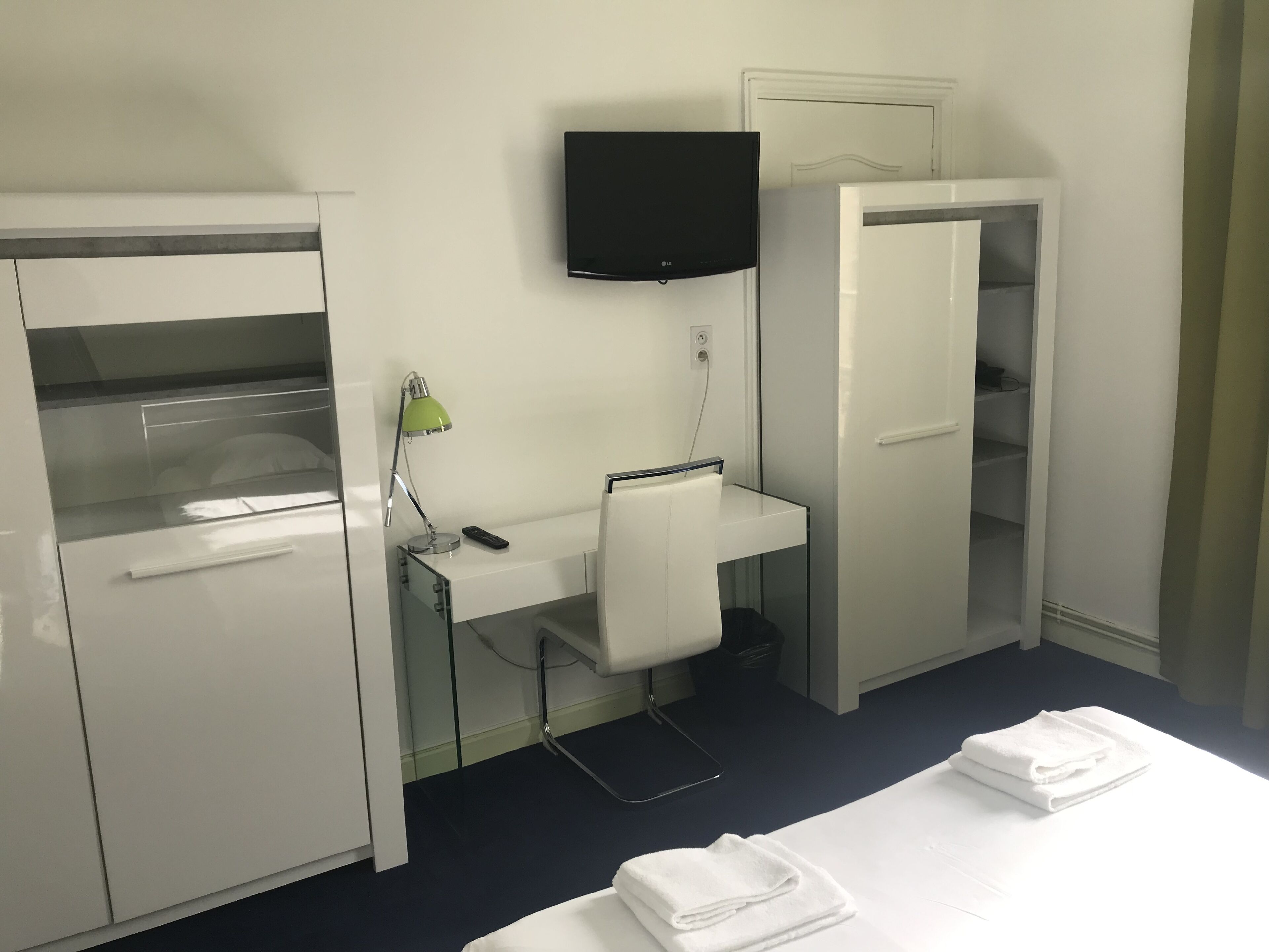 A hotel room with a bed, a desk with a chair, a television, and a wardrobe.