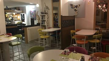 A dining area with round tables and chairs, a bar area in the background, and a wall with a colorful mural.