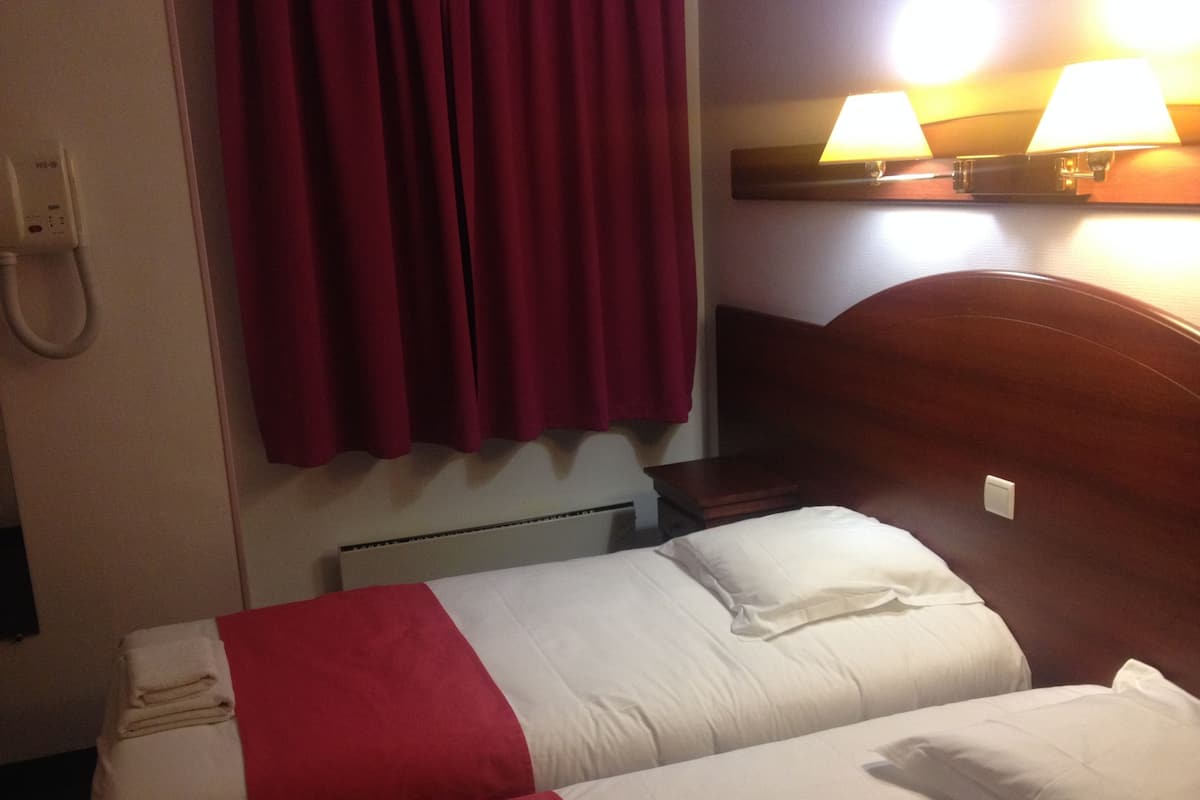 Une chambre d’hôtel avec deux lits, des rideaux rouges, une lampe fixée au mur et un téléphone.