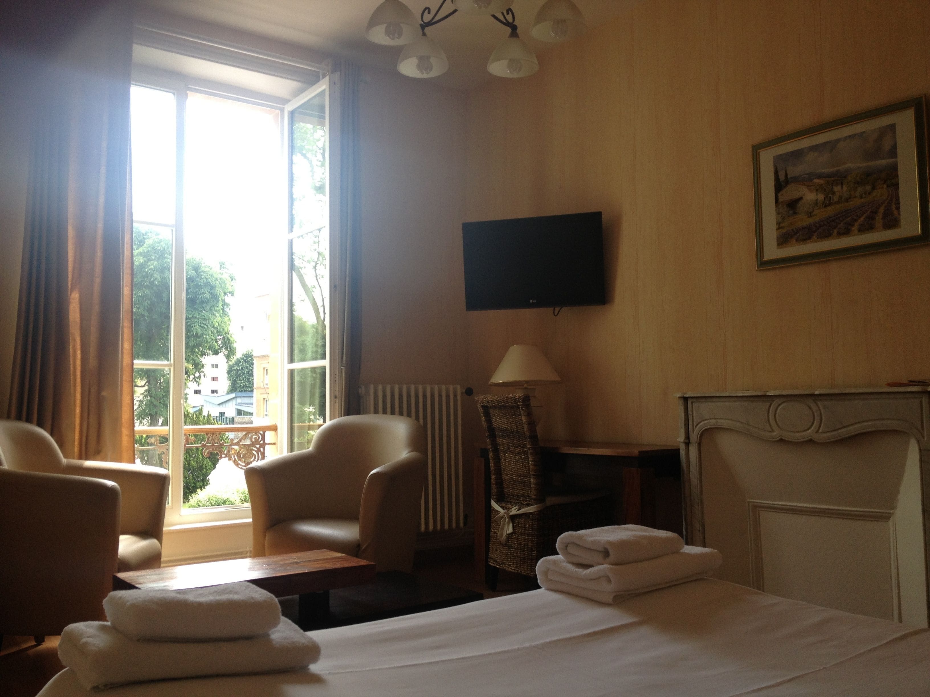 A hotel room with a bed, two armchairs, a table, a TV, and a fireplace.