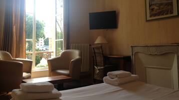 A hotel room with a bed, two armchairs, a table, a TV, and a fireplace.