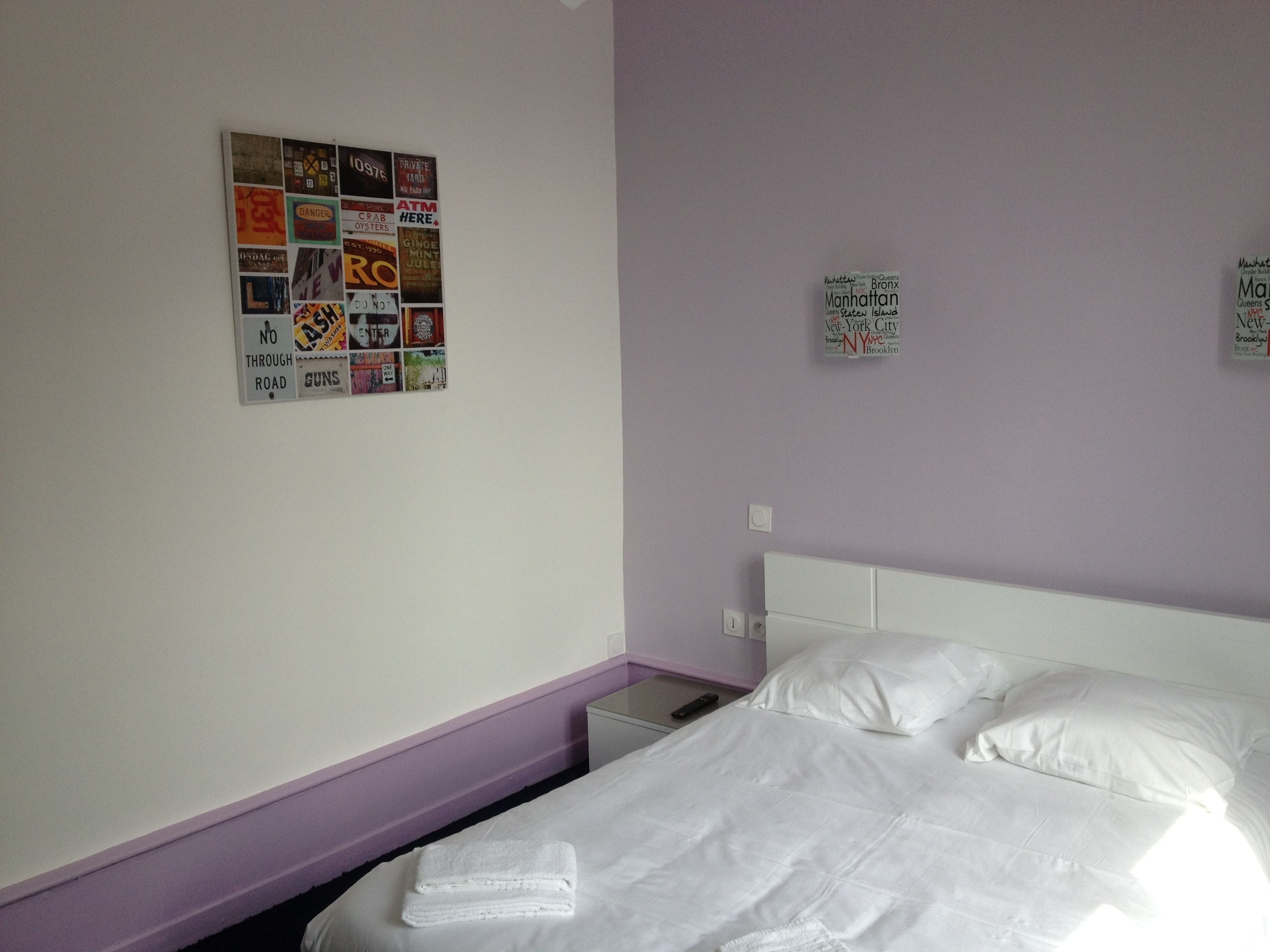 A hotel room with a bed, a nightstand, and a wall with various posters.
