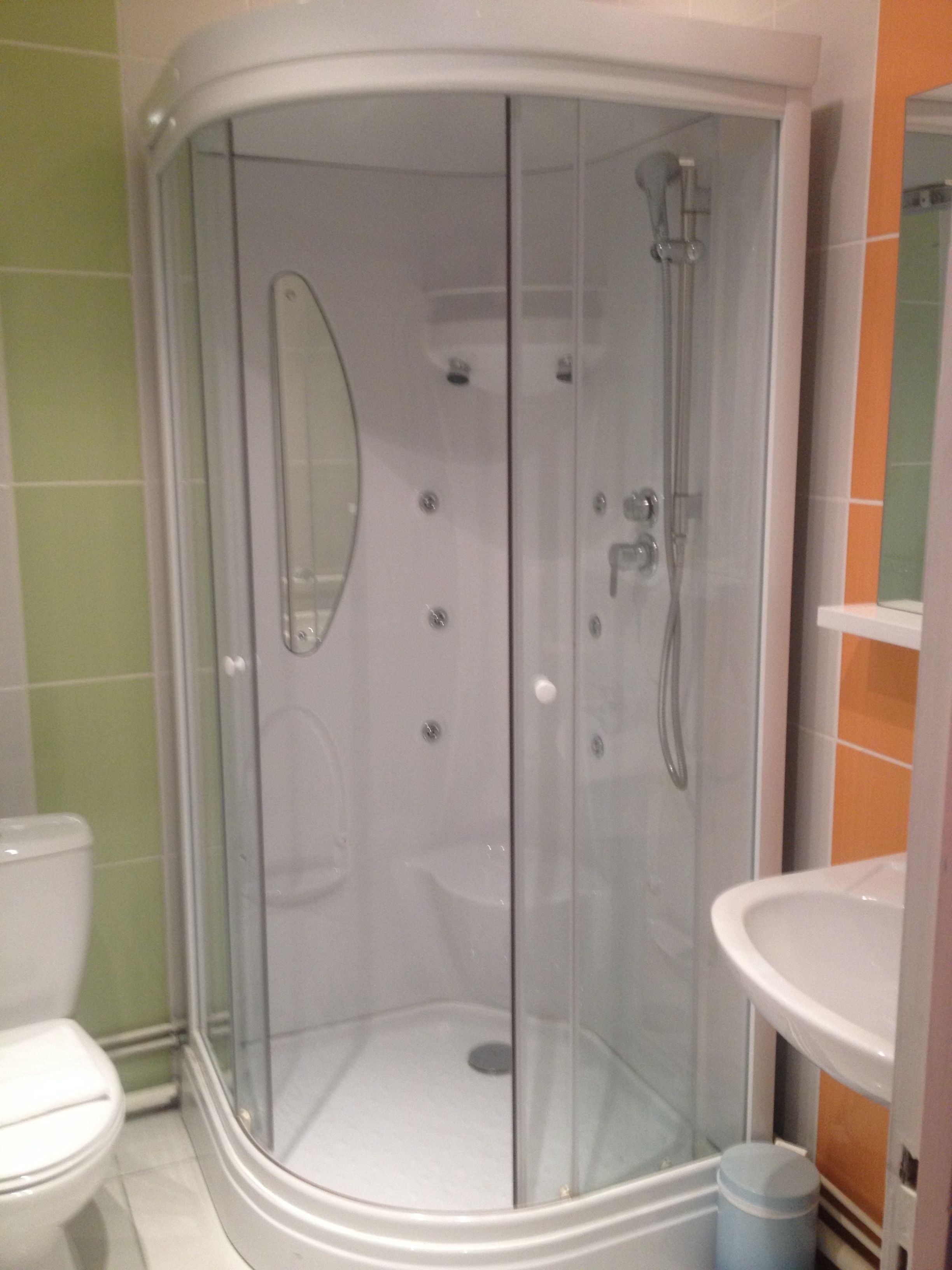A glass-enclosed shower stall with a white toilet and sink visible in the background.