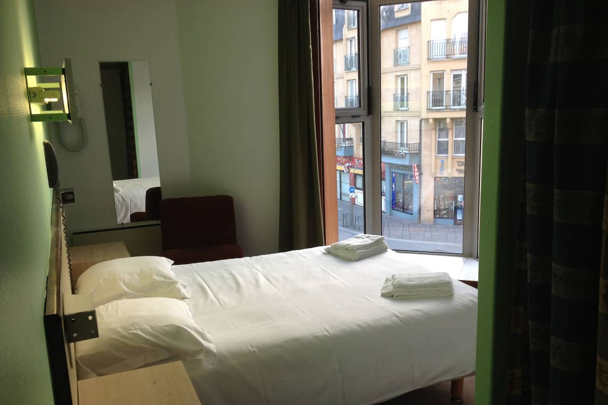Une chambre d’hôtel comprenant un lit, une chaise, un bureau, un téléphone et une fenêtre donnant sur des immeubles.