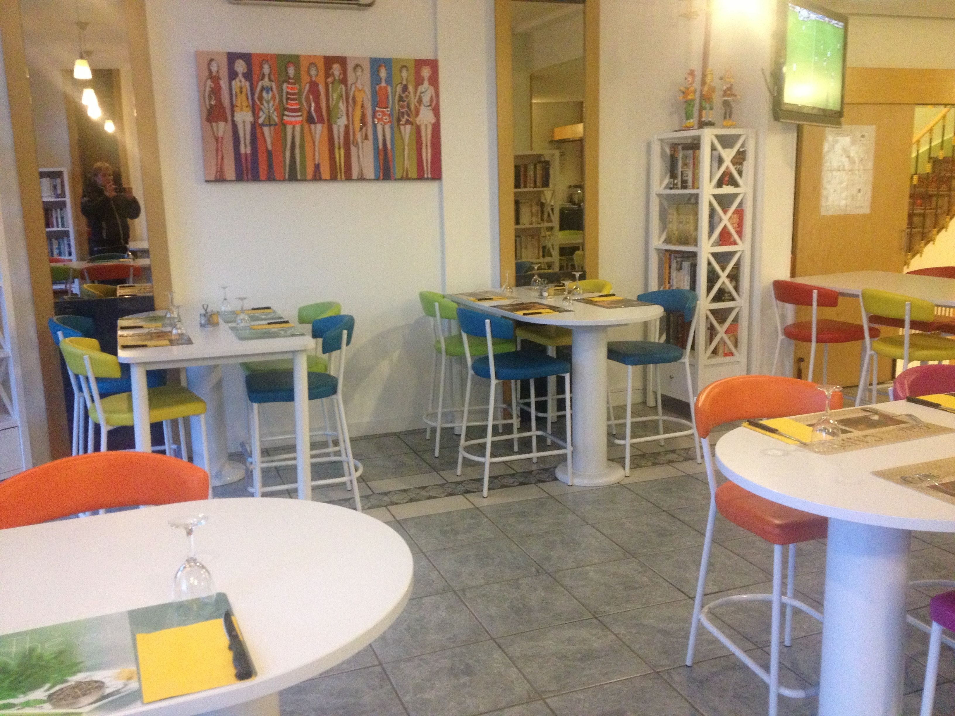 Interior de restaurante con varias mesas y sillas, un cuadro en la pared y un televisor montado.