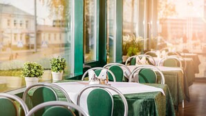 A restaurant with tables set for dining, potted plants, and a view of the street outside. - Hotel Zemaites (Vilnius)
