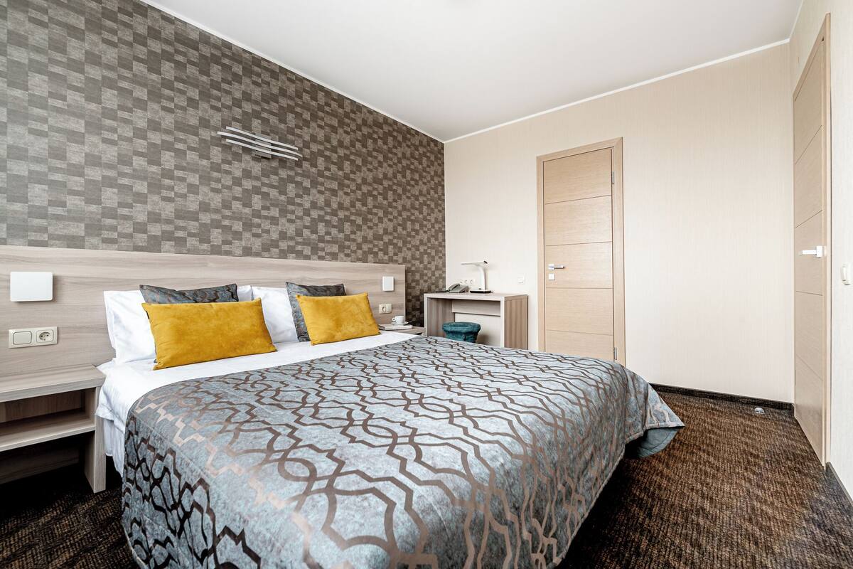 A hotel room with a large bed, a bedside table, a desk, and a wardrobe.