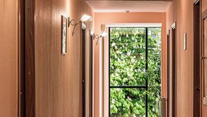A hallway with wooden doors, a tiled floor, and a large window with a view of greenery. - Hotel Zemaites (Vilnius)