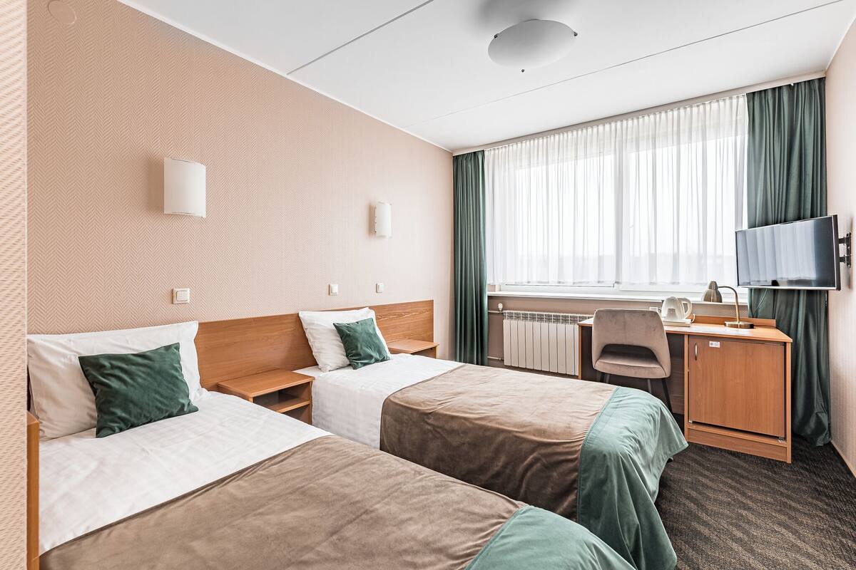 A hotel room with two beds, a desk, a chair, a television, and a window with curtains.