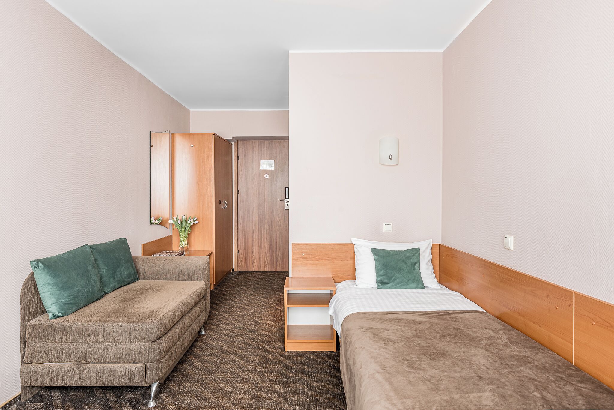 Une chambre d’hôtel avec deux lits simples, une armoire en bois, une petite table avec un vase et un miroir au mur.