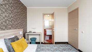 Habitación de hotel con cama, escritorio, espejo y baño visible a través de una puerta abierta.