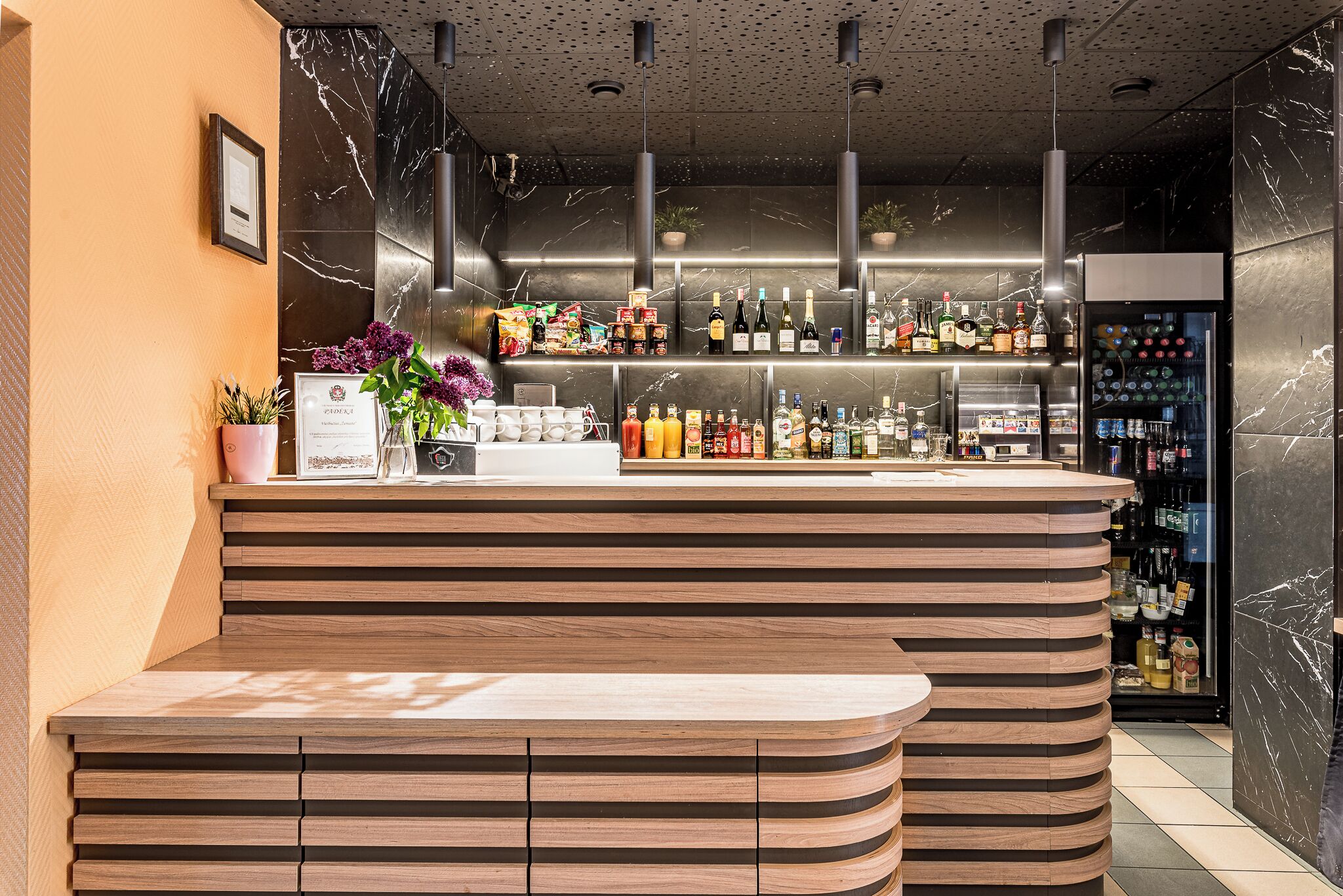 A bar area with a wooden counter, shelves with bottles, and a refrigerated display.