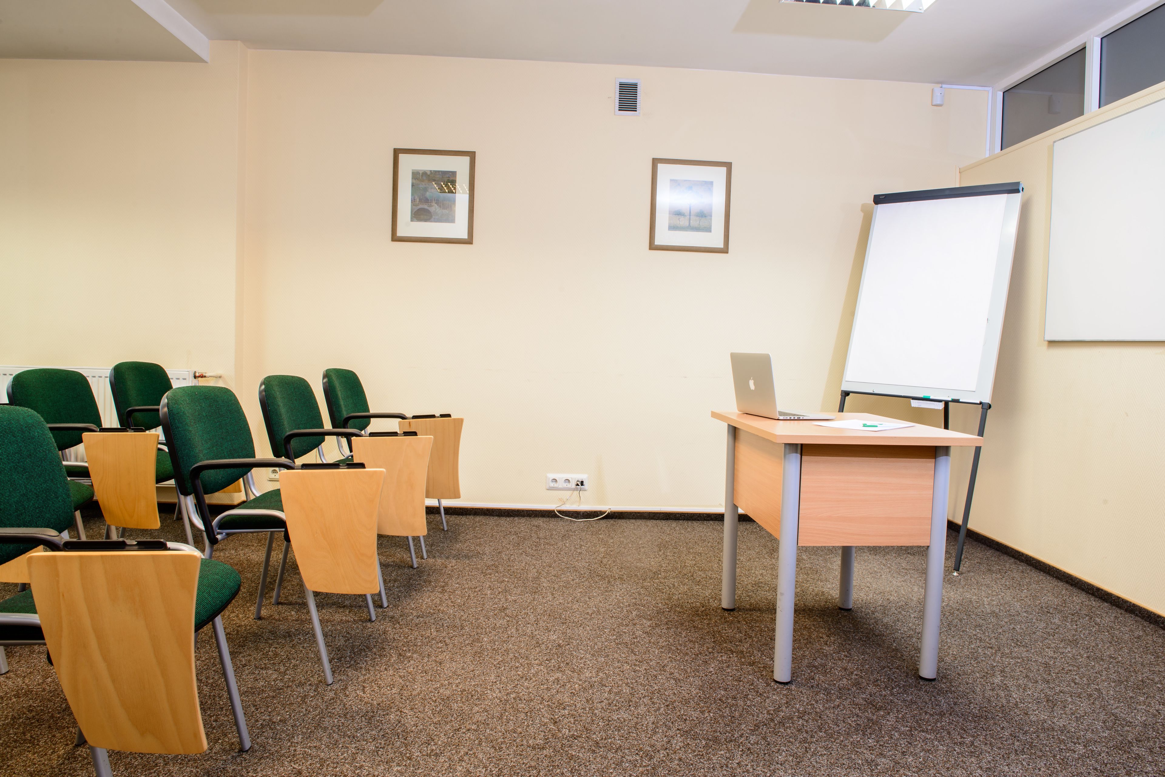A conference room with green chairs, a wooden desk, a laptop, and a whiteboard.