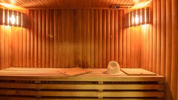 A sauna with wooden walls and benches, two wall-mounted light fixtures, and a wooden cutting board and hat on the benches.