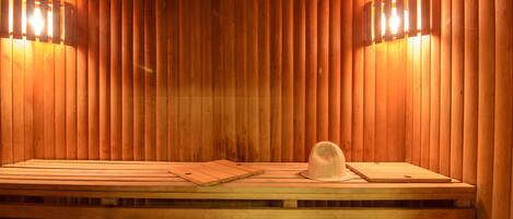 A sauna with wooden walls and benches, two wall-mounted light fixtures, and a wooden cutting board and hat on the benches.