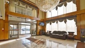 A spacious lobby with a grand chandelier, a seating area with sofas, and a large window with curtains. - Woodbine Hotel and Suites (Toronto)