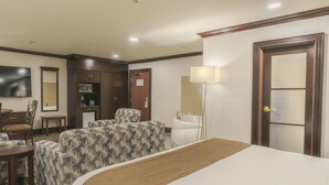 A hotel room with a bed, two patterned chairs, a small table, a microwave, a refrigerator, a bathroom with a toilet and sink, and a TV. - Woodbine Hotel and Suites (Toronto)