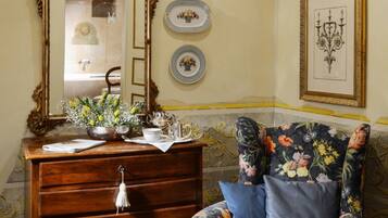 A room with a wooden dresser, a floral armchair, a mirror, and decorative plates on the wall.