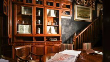 A wooden bookcase with glass doors, a wooden desk with a book, and a staircase with a chandelier.