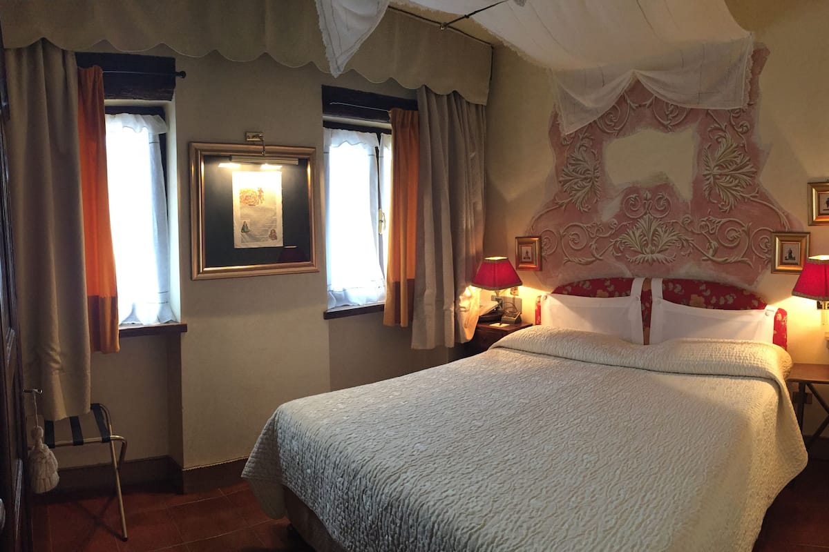 A bedroom with a large bed, two bedside lamps, a framed picture on the wall, and a window with curtains.