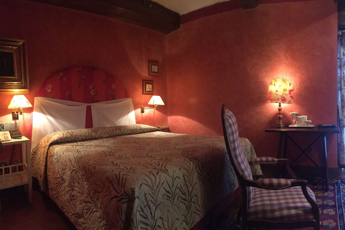 A hotel room with a large bed, two bedside lamps, a chair, and a small table with a lamp.