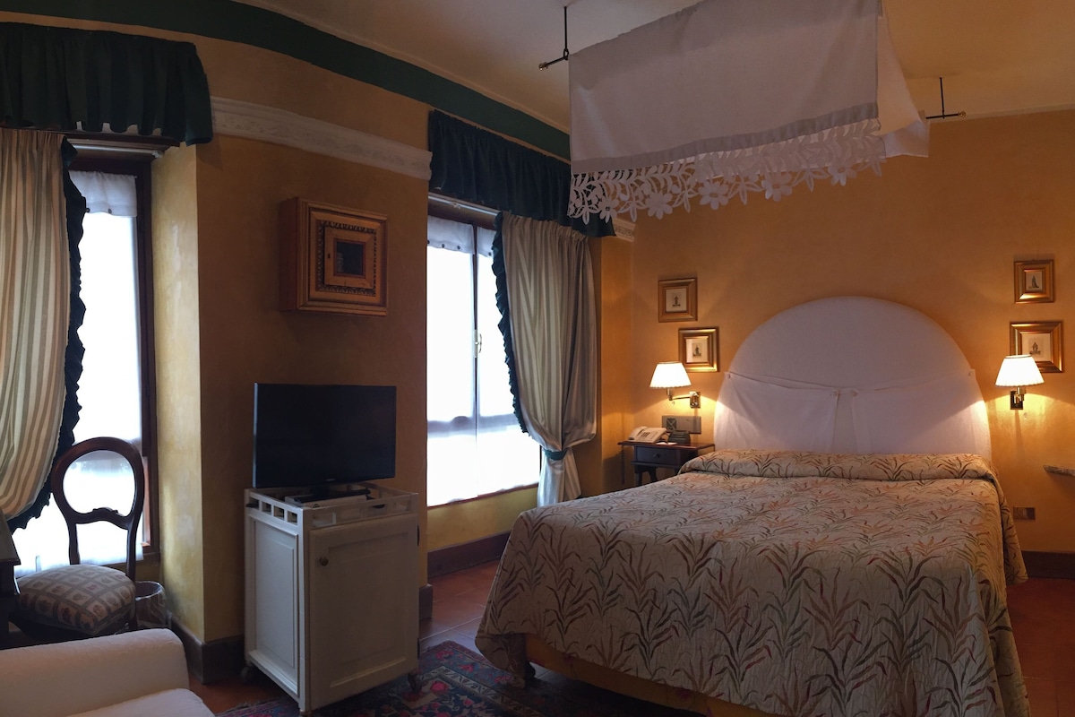 A hotel room with a bed, a desk with a television, a chair, and a window with curtains.