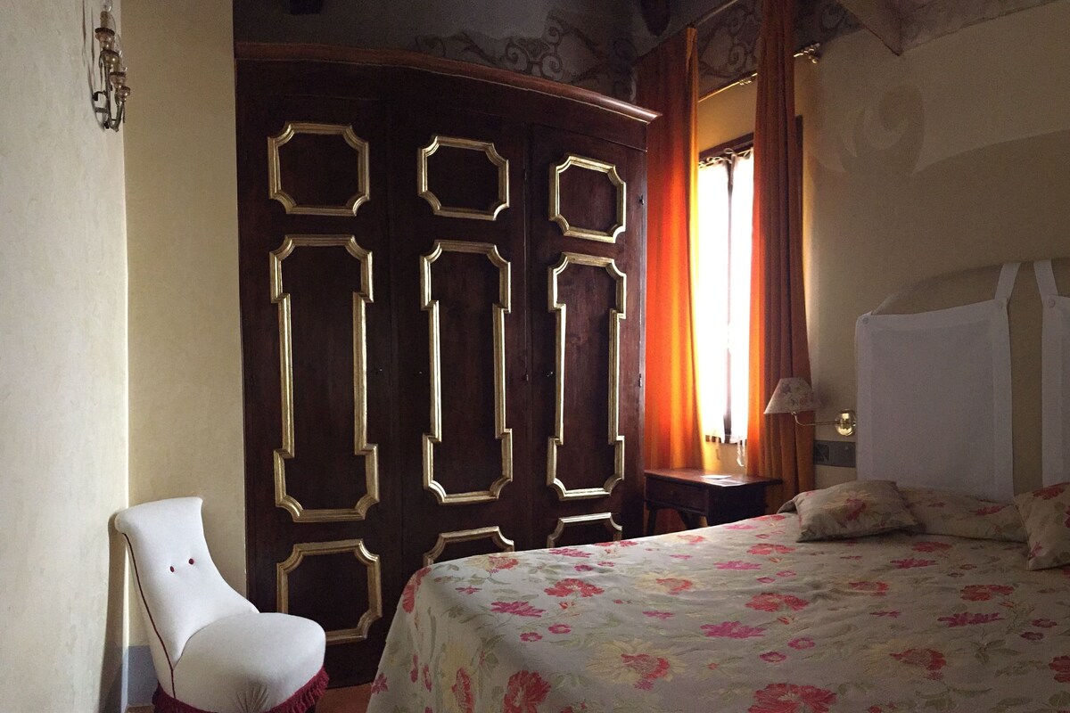 A bedroom with a bed, a chair, a wardrobe, and a window with curtains.