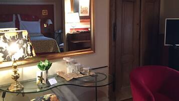 A hotel room with a bed, a glass table with decorative items, a red armchair, and a large mirror reflecting the room.