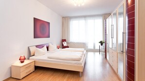 Un dormitorio moderno con cama, mesitas de noche, una silla roja, un espejo grande y un ventanal con cortinas.