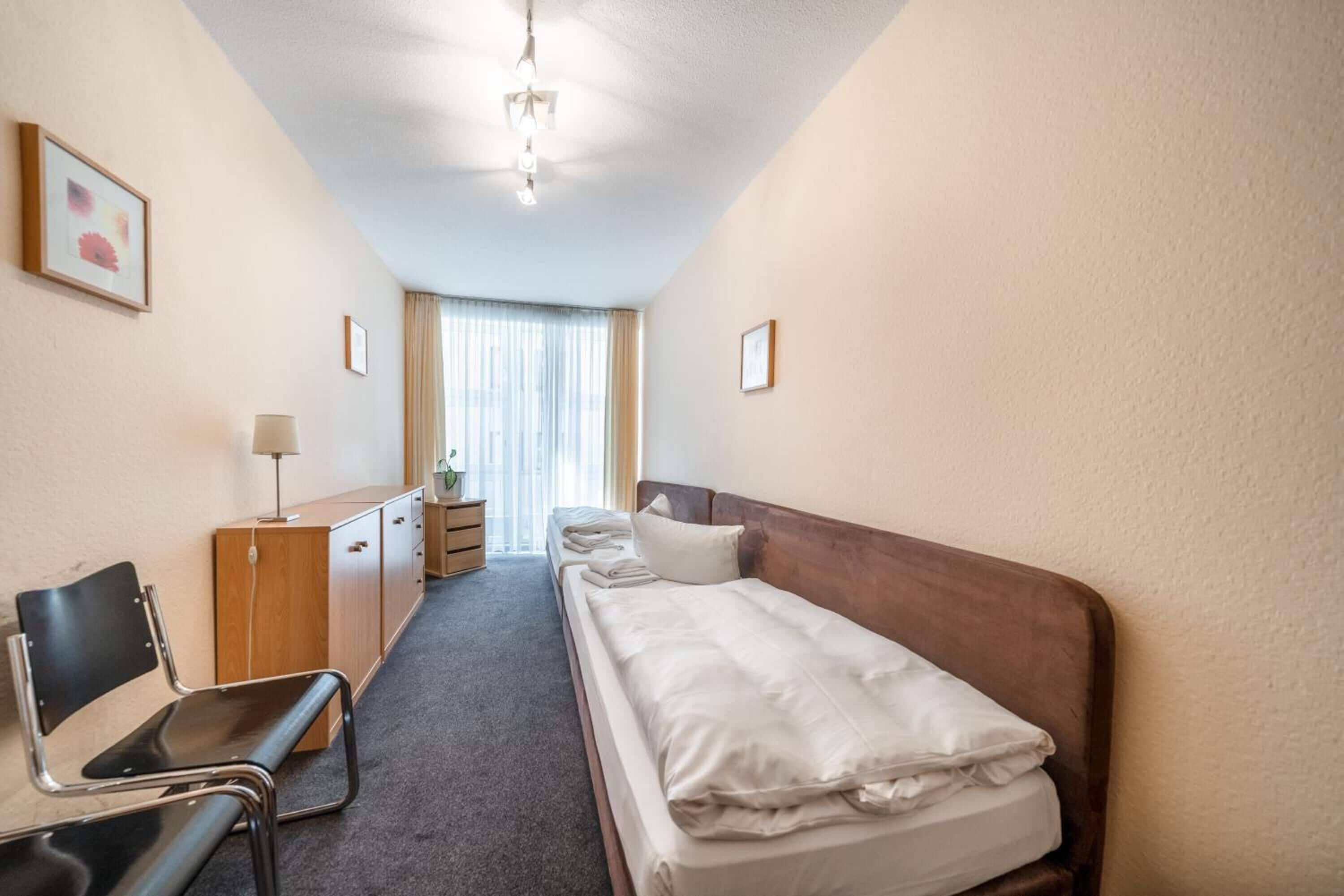 Een hotelkamer met een bed, een bureau, een stoel en een raam met gordijnen.